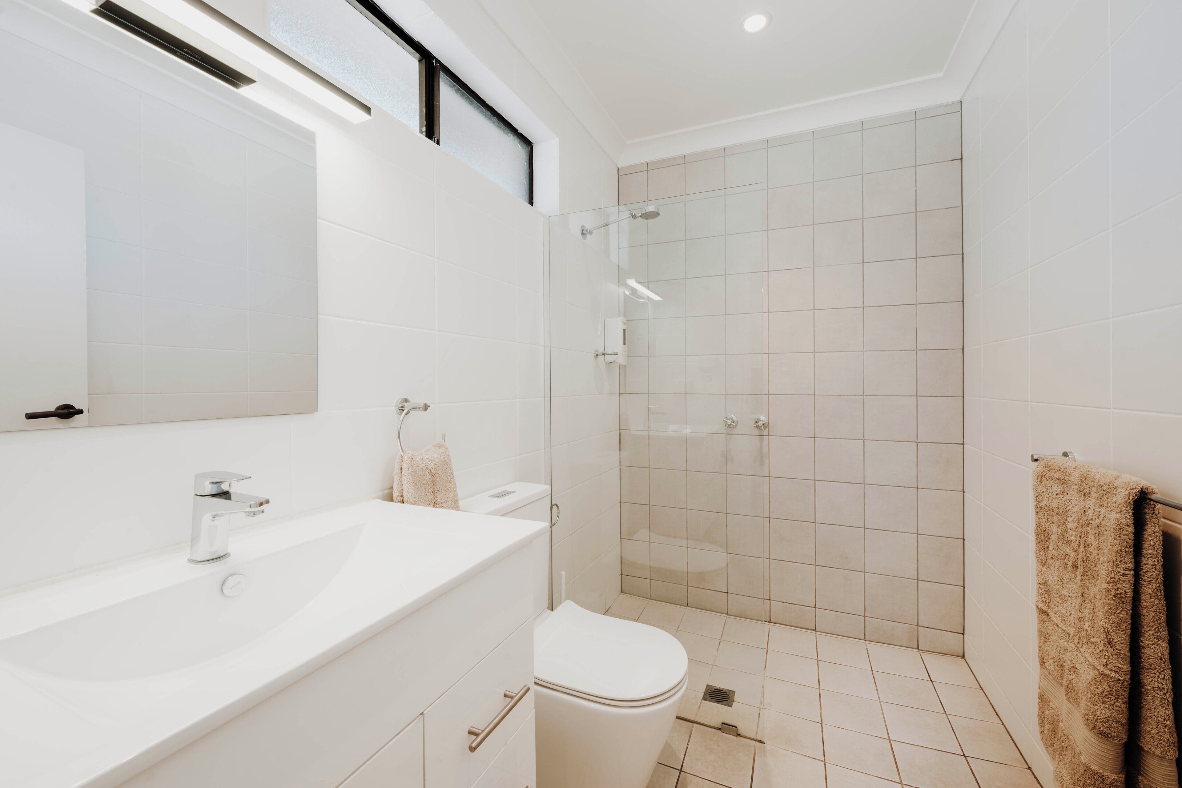 Un baño moderno con lavamanos, inodoro y zona de ducha blancos.