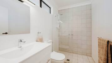 Un baño moderno con lavamanos, inodoro y zona de ducha blancos.