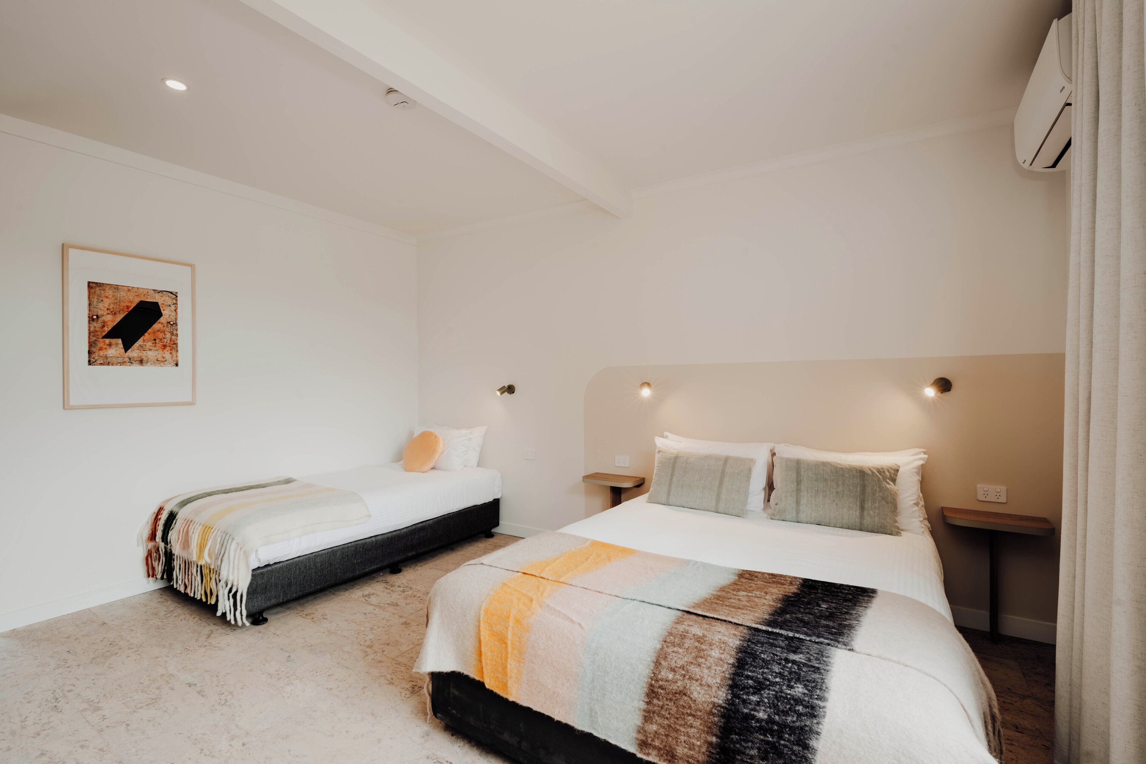 A hotel room with two beds, a large window, and a wall-mounted air conditioner.