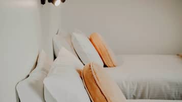 A neatly made bed with white and orange pillows, a black wall-mounted lamp, and a plain white wall.