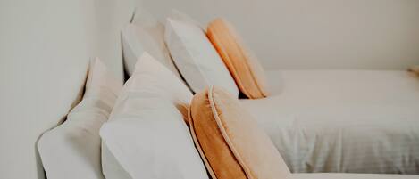 A neatly made bed with white and orange pillows, a black wall-mounted lamp, and a plain white wall.
