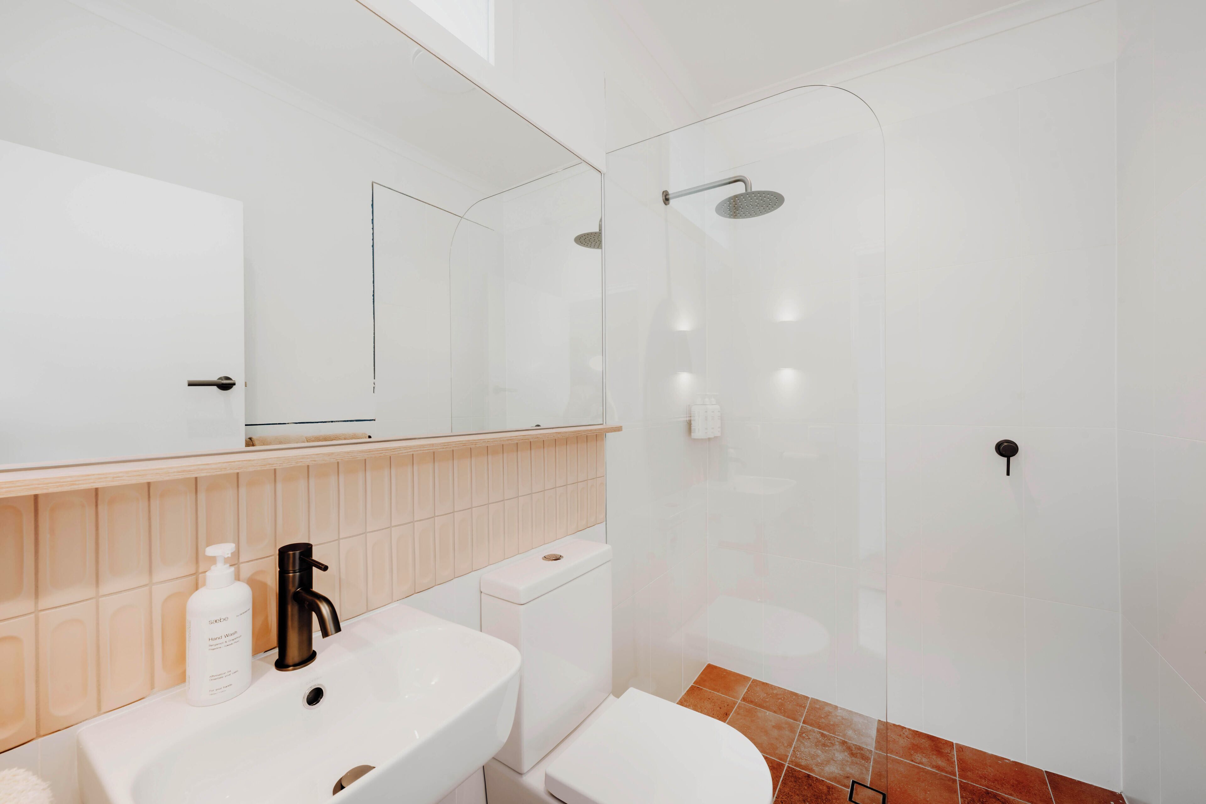 Un baño moderno con un lavabo blanco, un inodoro y una zona de ducha con mampara de vidrio.