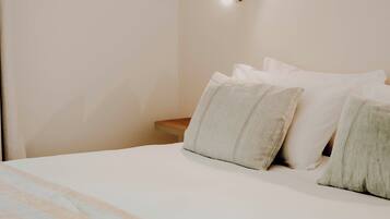 A neatly made bed with a striped blanket and pillows, a bedside table with a lamp, and a plain wall.