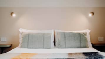 Una cama bien hecha con dos almohadas y una manta, una mesita de noche y un enchufe de pared.