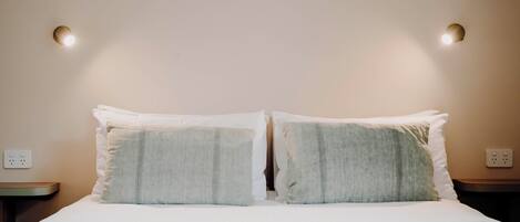 A neatly made bed with two pillows and a blanket, a bedside table, and a wall socket.