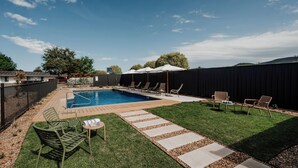 Un patio trasero con piscina, sillas de descanso y una terraza de madera.