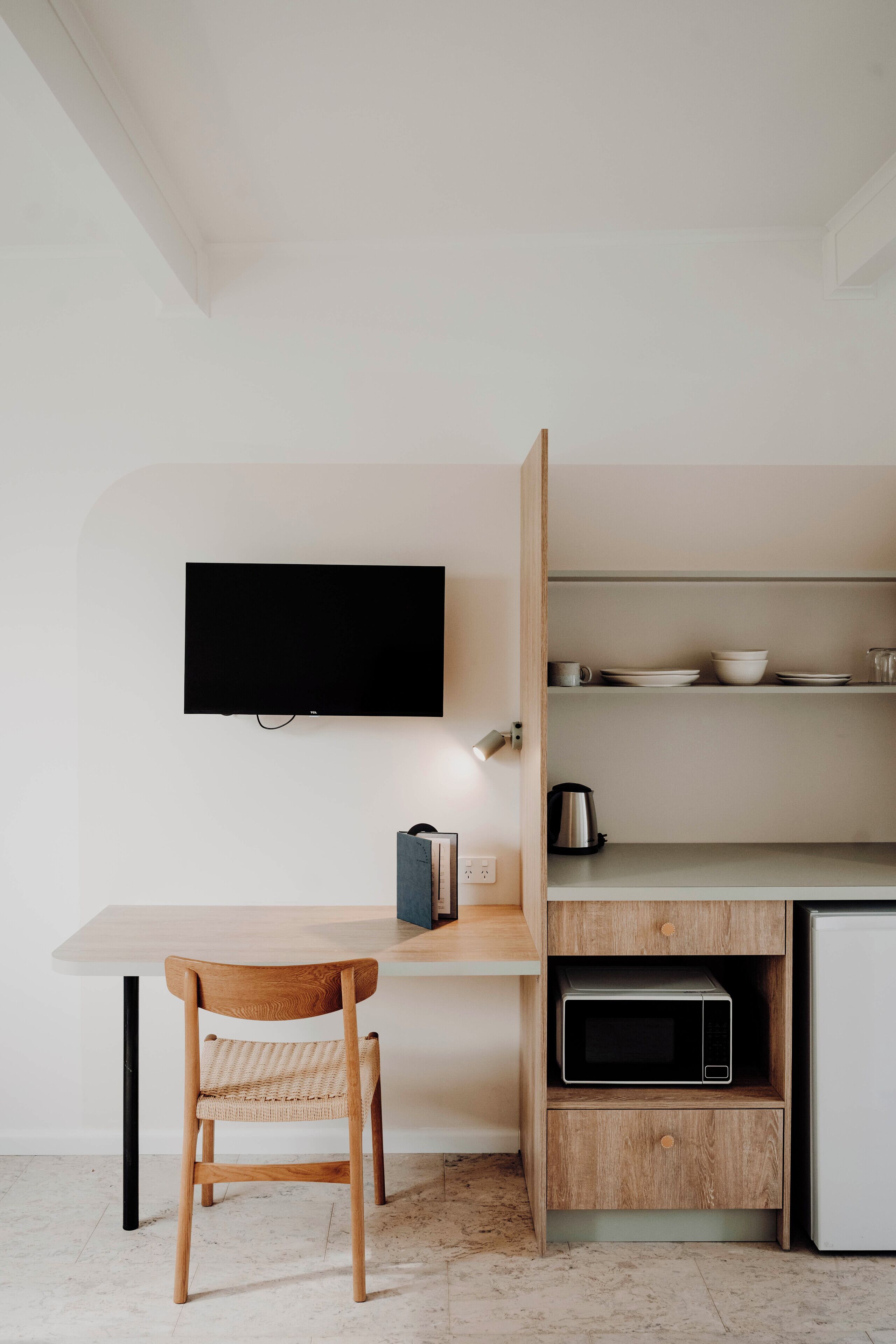 Una cocina moderna con una mesa de madera, un televisor montado en la pared y estantes empotrados con utensilios de cocina.
