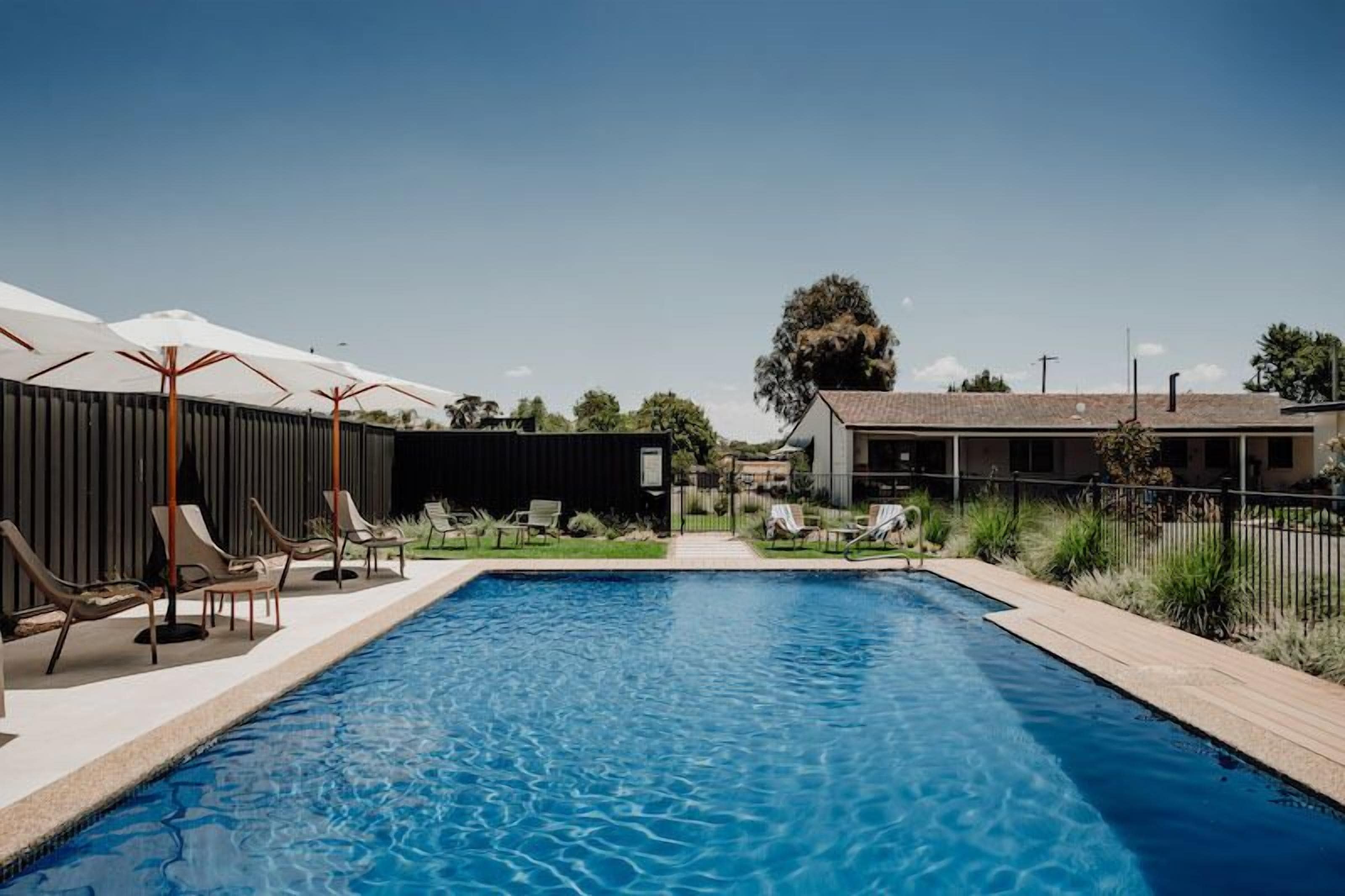Piscina com espreguiçadeiras e guarda-sóis, cercada por cerca e vegetação.