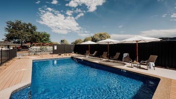 Una piscina al aire libre, sombrillas, sillones reclinables de piscina