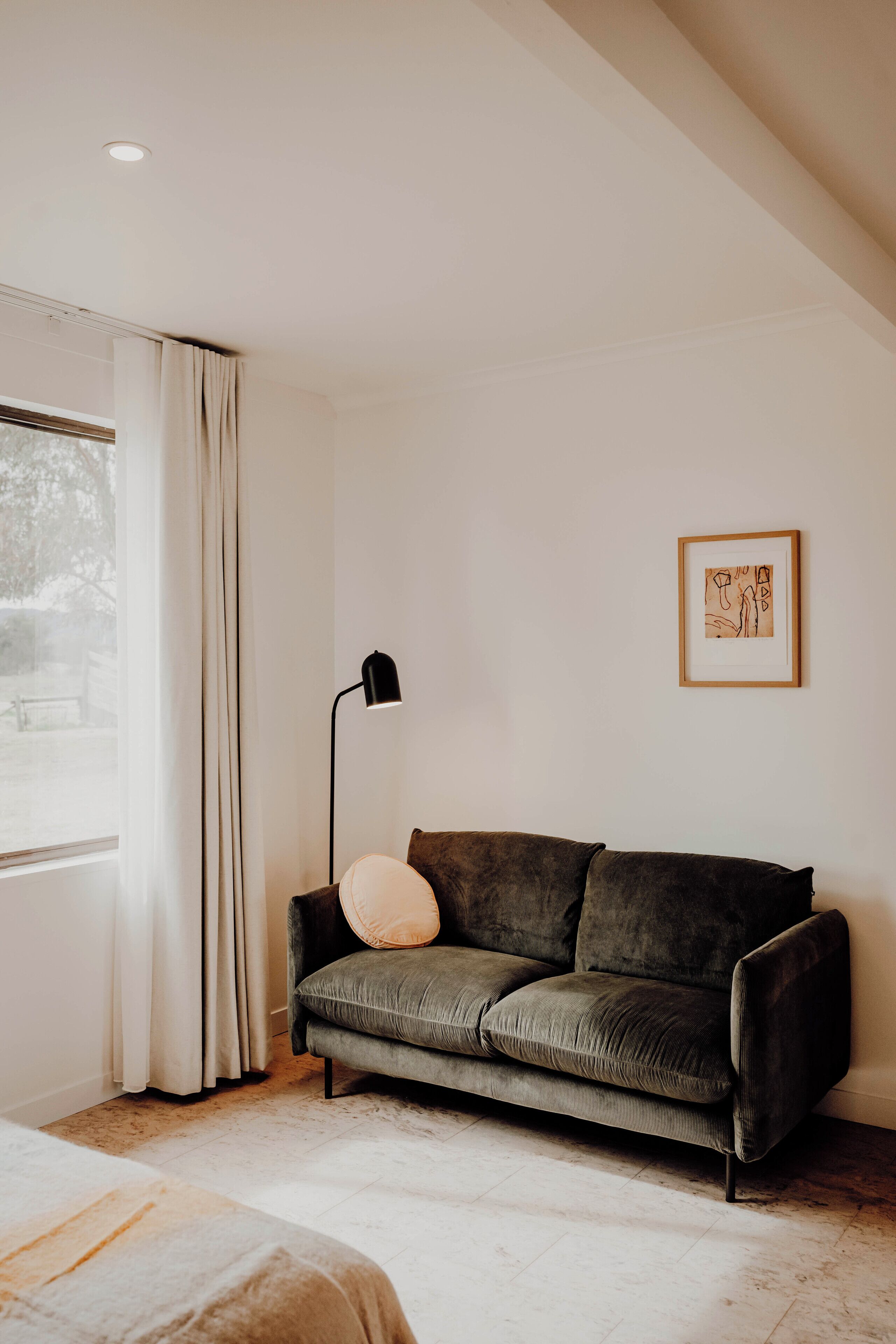 Una habitación moderna con un sofá verde oscuro, una lámpara de pie y un cuadro en la pared.