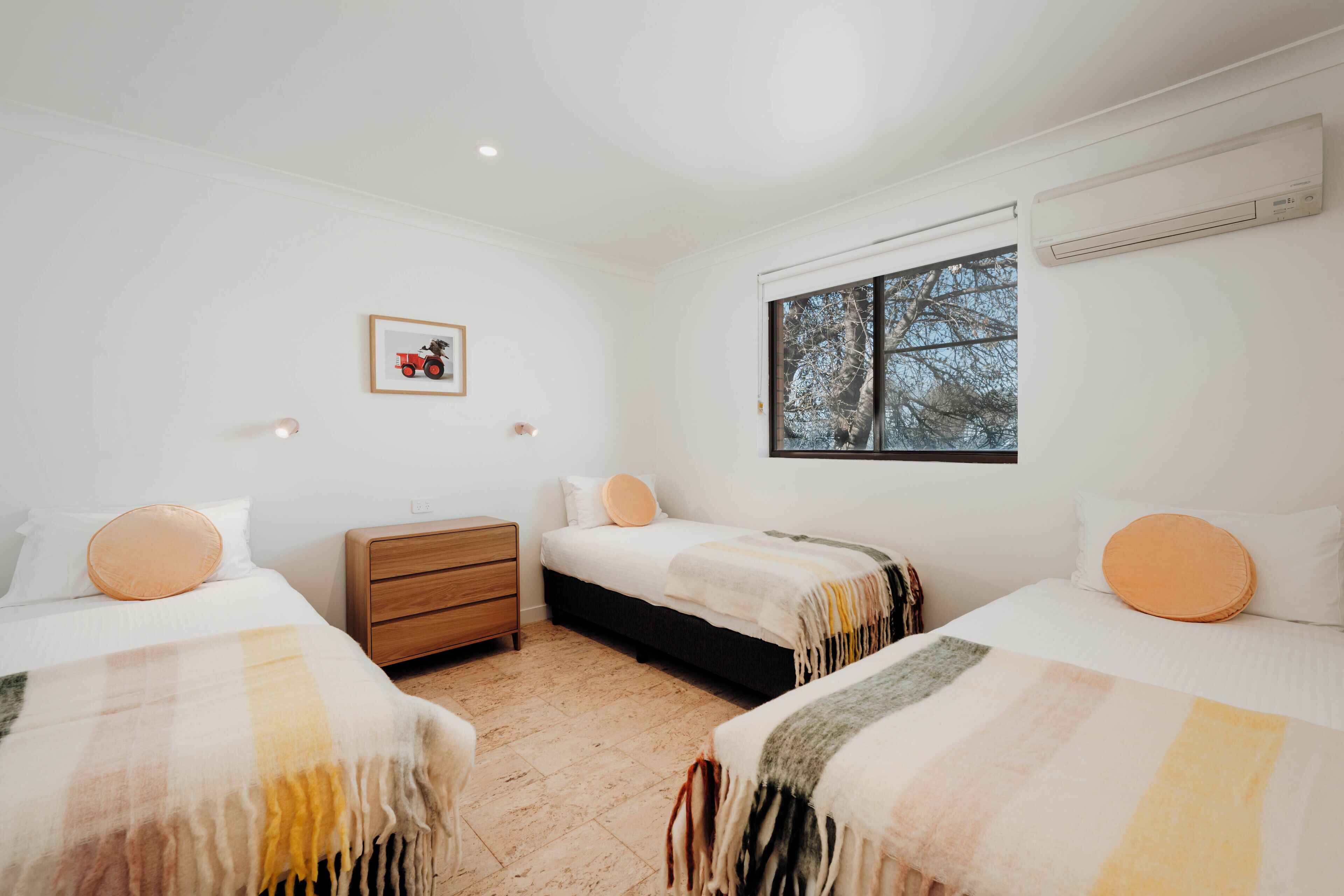 A bedroom with two beds, a nightstand, and a window with a view of trees.