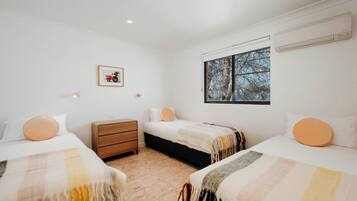 A bedroom with two beds, a nightstand, and a window with a view of trees.