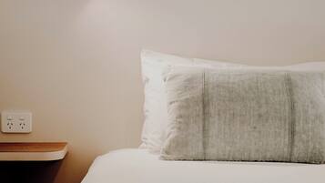 Uma cama bem arrumada com um edredom listrado, um travesseiro branco e um luminário fixado na parede.