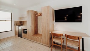 Una cocina moderna con armarios de madera, microondas integrado y un refrigerador pequeño. Hay un comedor con una mesa y dos sillas.