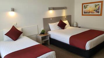 A hotel room with two beds, each with a red and white bedspread, a nightstand with a lamp, and a small plant.