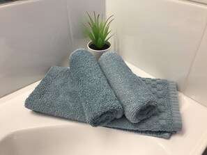 A bathroom with a white bathtub, a potted plant, and two folded towels.
