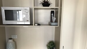 Une petite cuisine équipée d’un four à micro-ondes, d’un petit réfrigérateur, d’un évier et d’une étagère sur laquelle est posée une plante en pot.