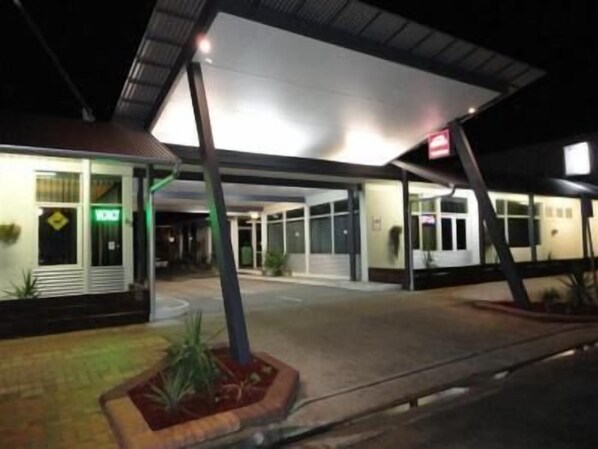 A hotel entrance with a covered walkway, a visible exit sign, and a small garden area with plants.