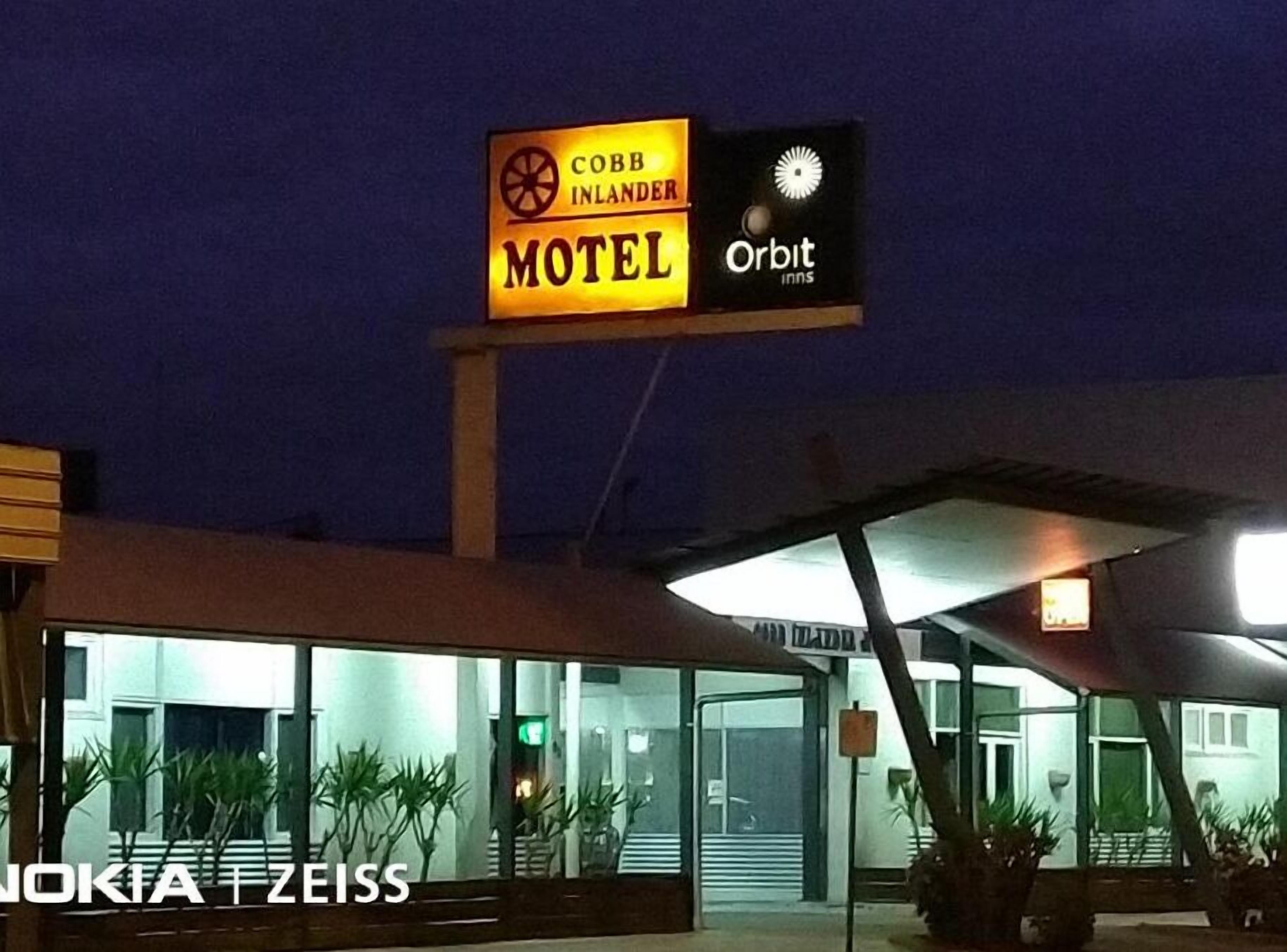 Ein Schild mit den Logos 'Cobb Inlander' und 'Orbit Inns', ein moderner Gebäudeeingang und Zimmerpflanzen.