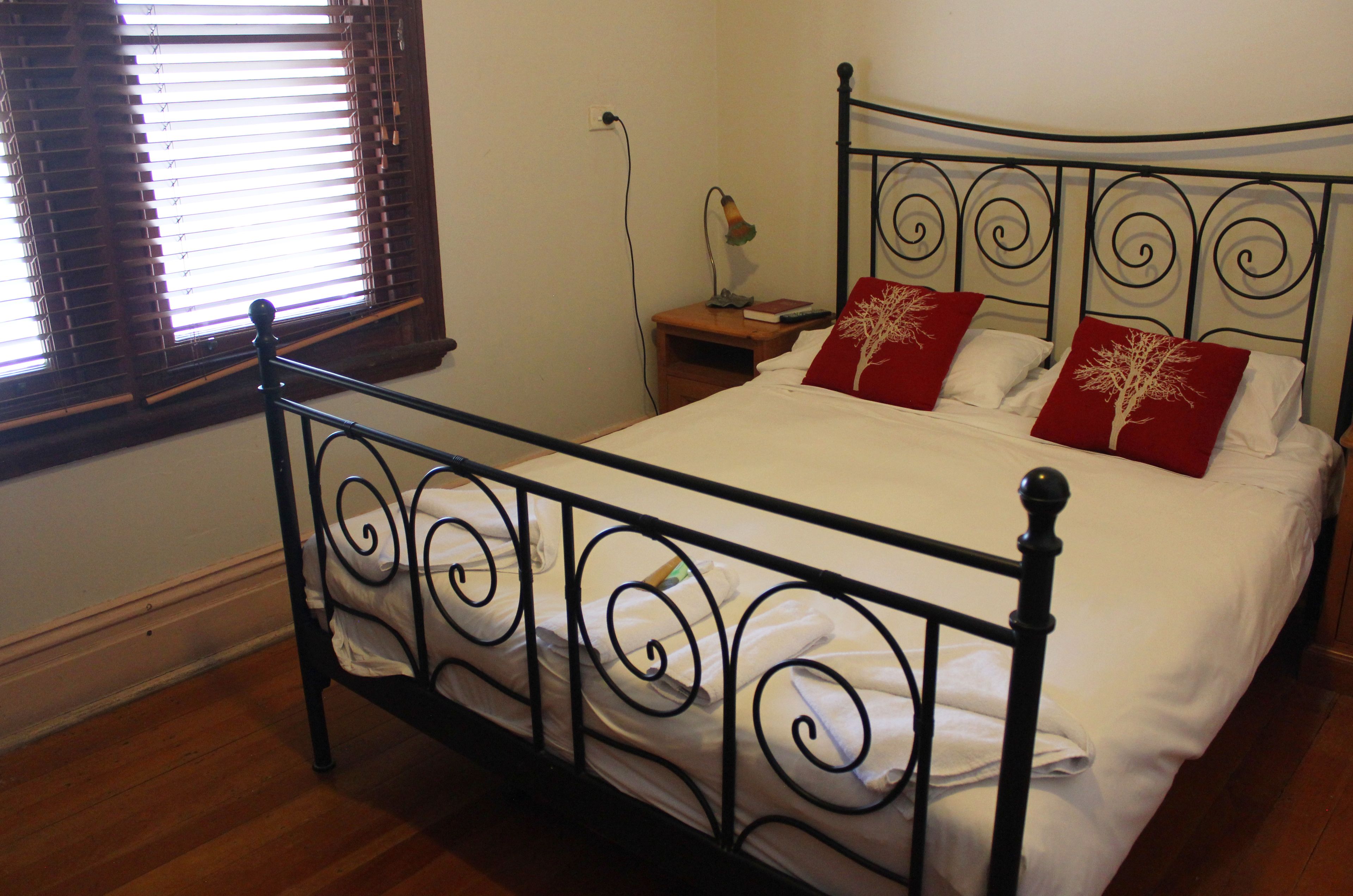 A neatly made bed with white linens and two red pillows with a tree design, a bedside lamp, and a wooden nightstand.