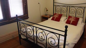 A neatly made bed with white linens and two red pillows with a tree design, a bedside lamp, and a wooden nightstand.