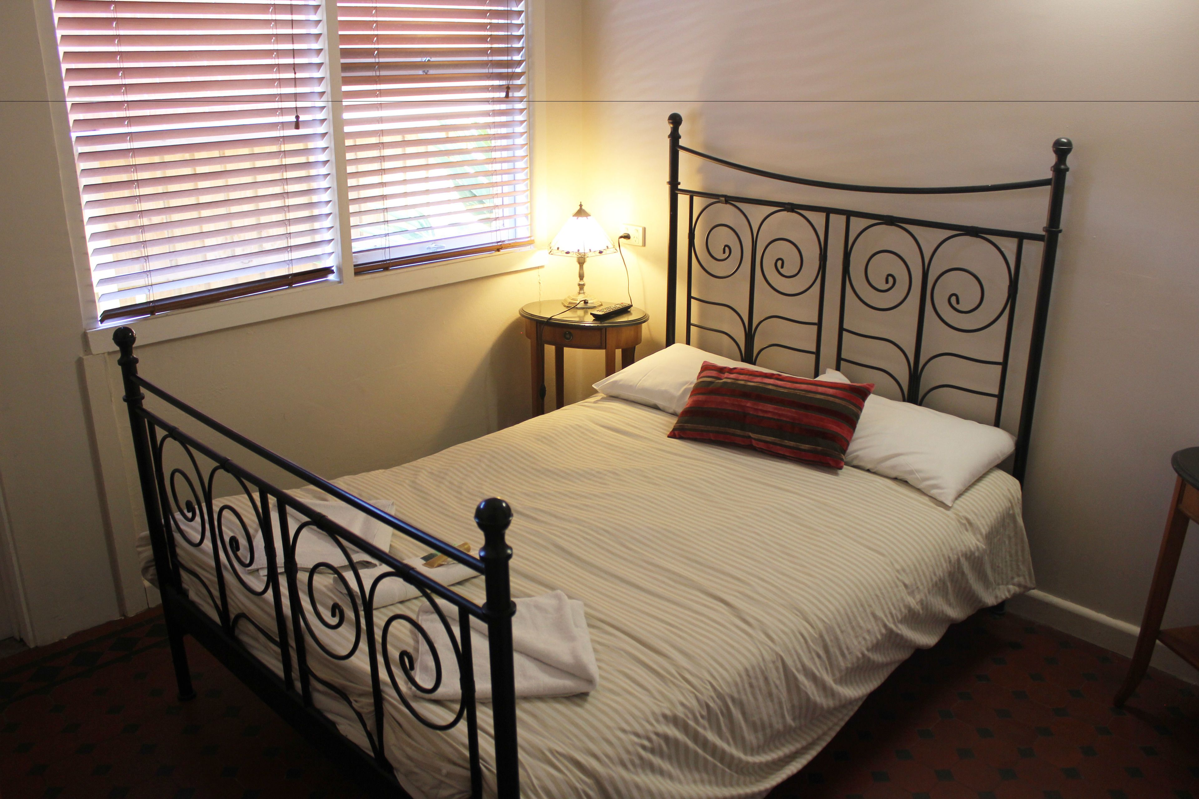 A single bed with a metal frame, a bedside table with a lamp, and a window with blinds.