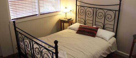 A single bed with a metal frame, a bedside table with a lamp, and a window with blinds.