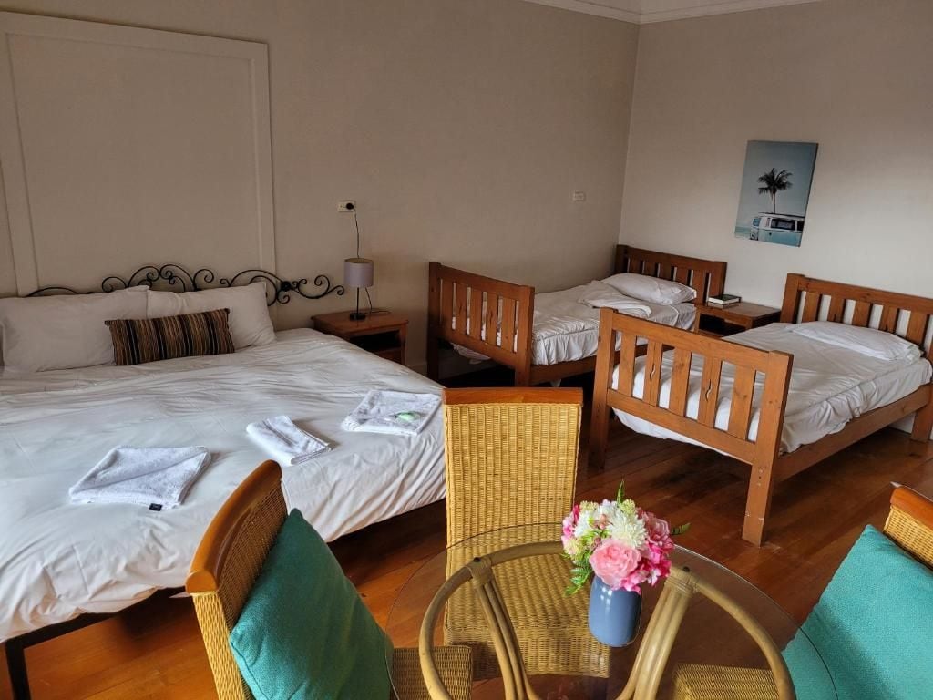 A hotel room with two single beds, a small round table with a vase of flowers, and a wicker chair.