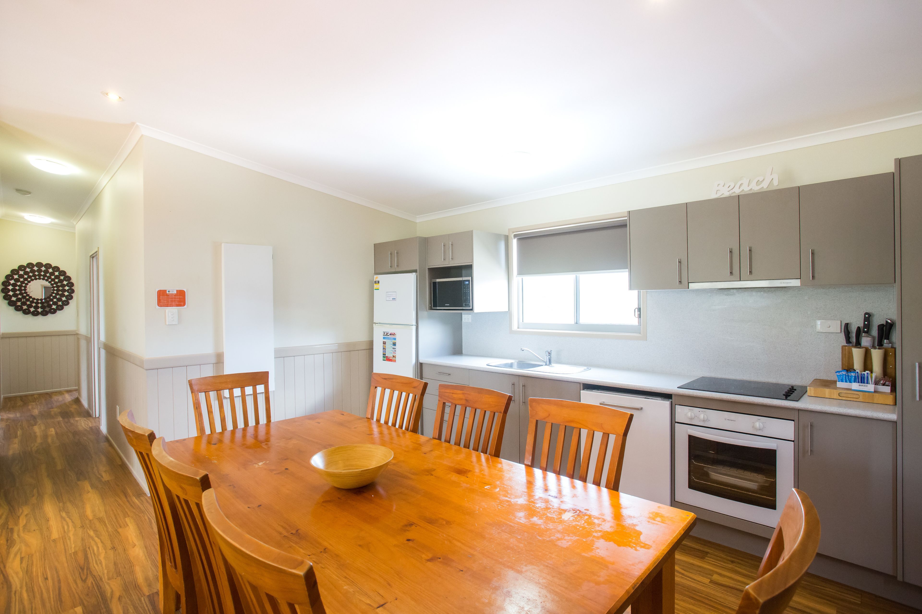 A modern kitchen with white cabinets, a wooden dining table, and a built-in oven.