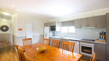 A modern kitchen with white cabinets, a wooden dining table, and a built-in oven.