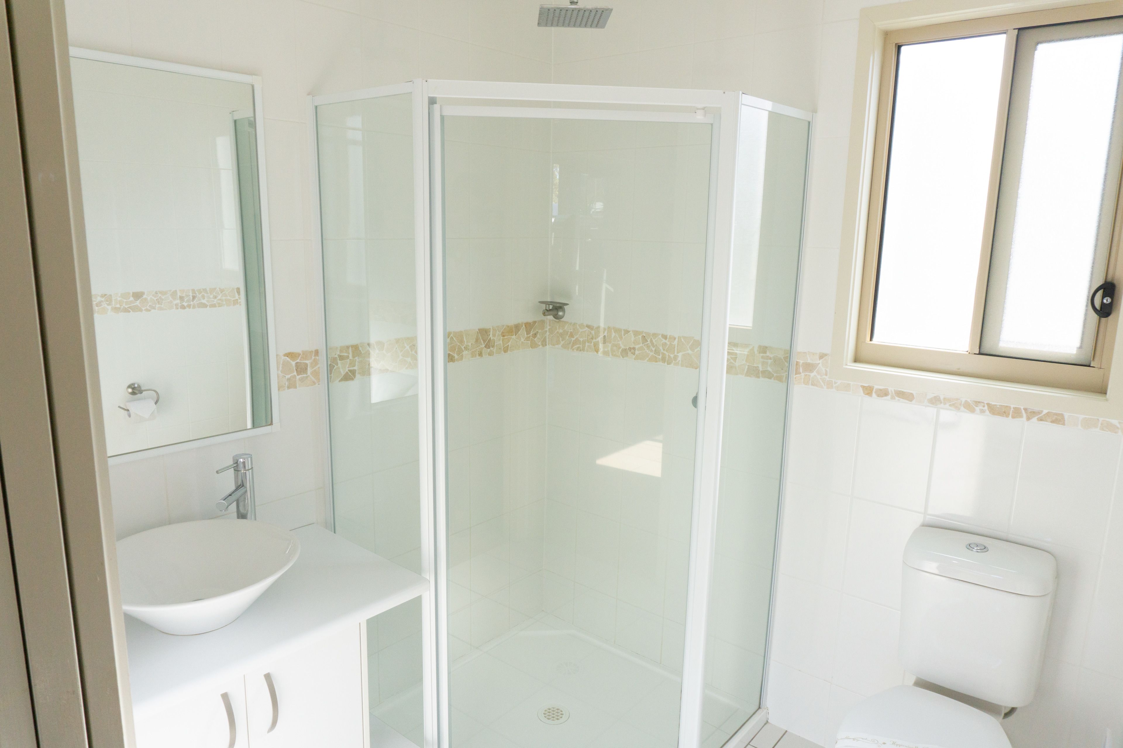 Un baño con ducha de vidrio, lavamanos blanco y retrete.