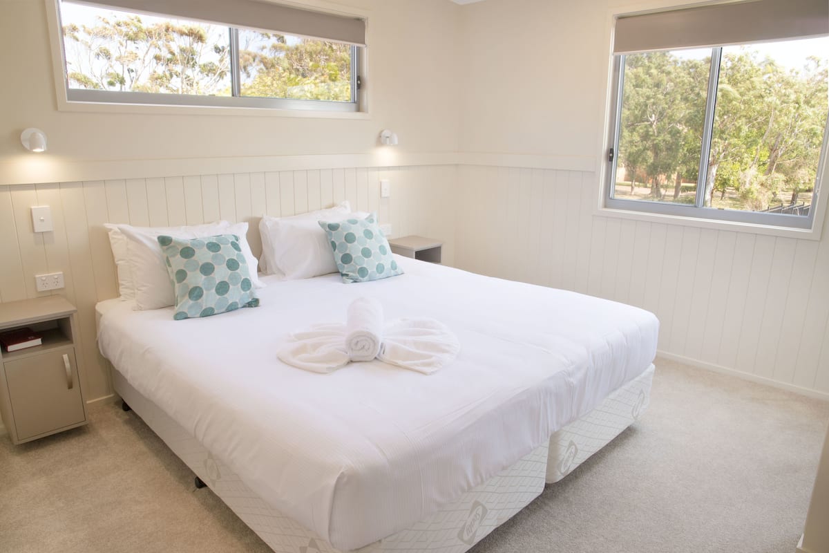 A neatly made bed with white bedding and blue polka dot pillows, a small bedside table, and a nightstand with a book on it.