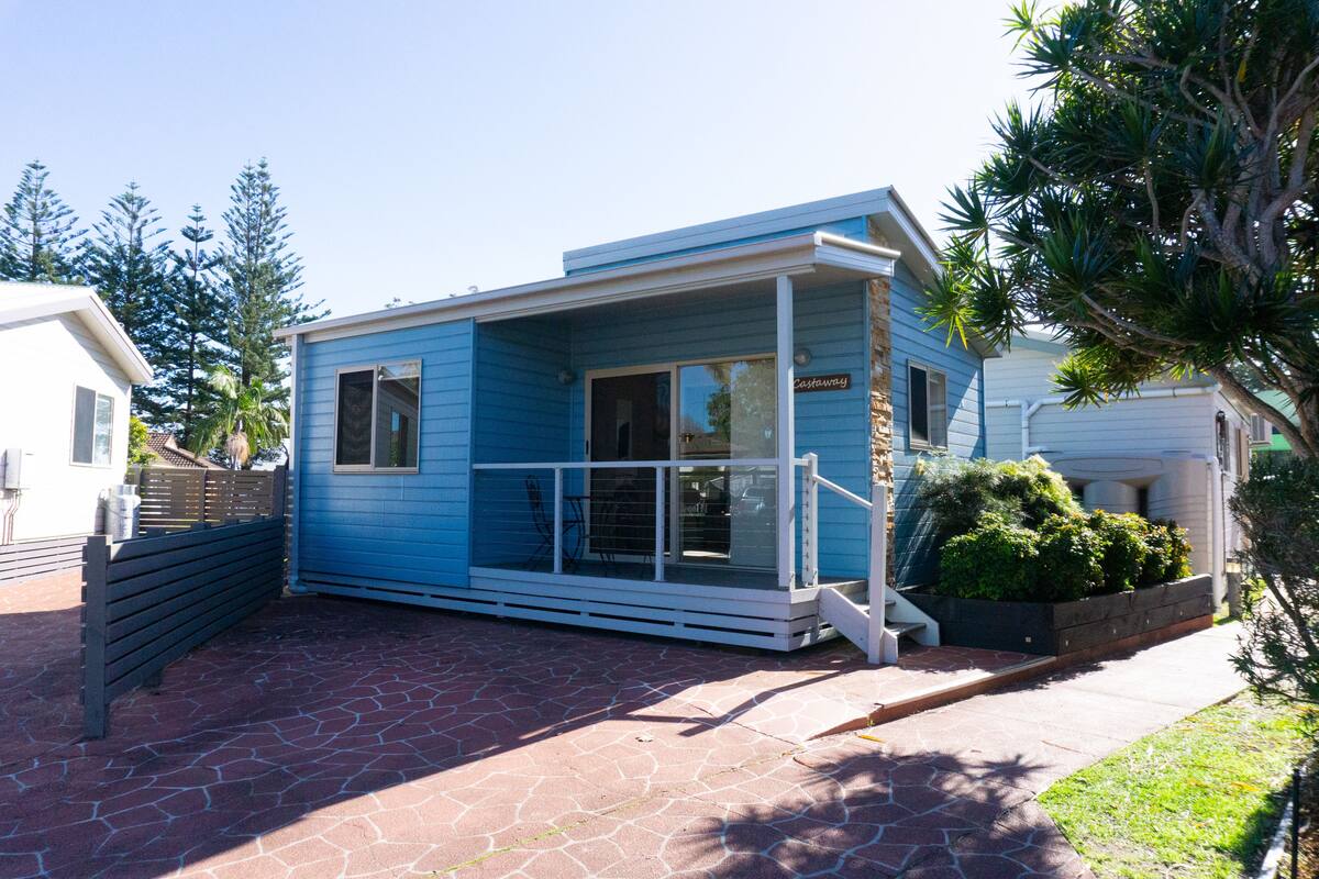 A small, single-story blue house with a porch and a covered entryway.