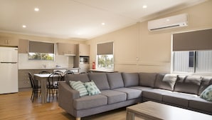 Una sala de estar moderna con un sofá seccional gris, una mesa de centro de madera y un comedor con una mesa y sillas blancas.