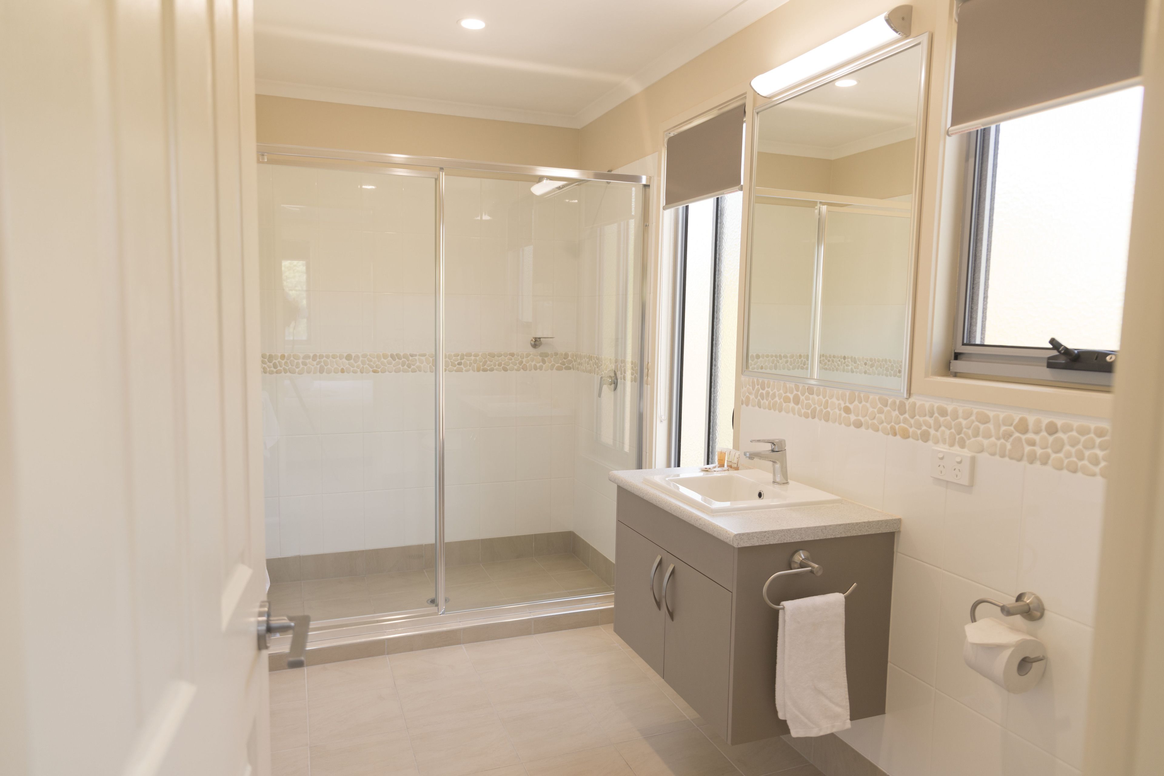 Une salle de bain moderne avec une douche à parois de verre, un lavabo avec un miroir et une serviette accrochée au mur.
