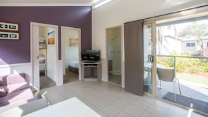 Una sala de estar moderna con televisor, sofá y puerta de vidrio que da a un balcón.