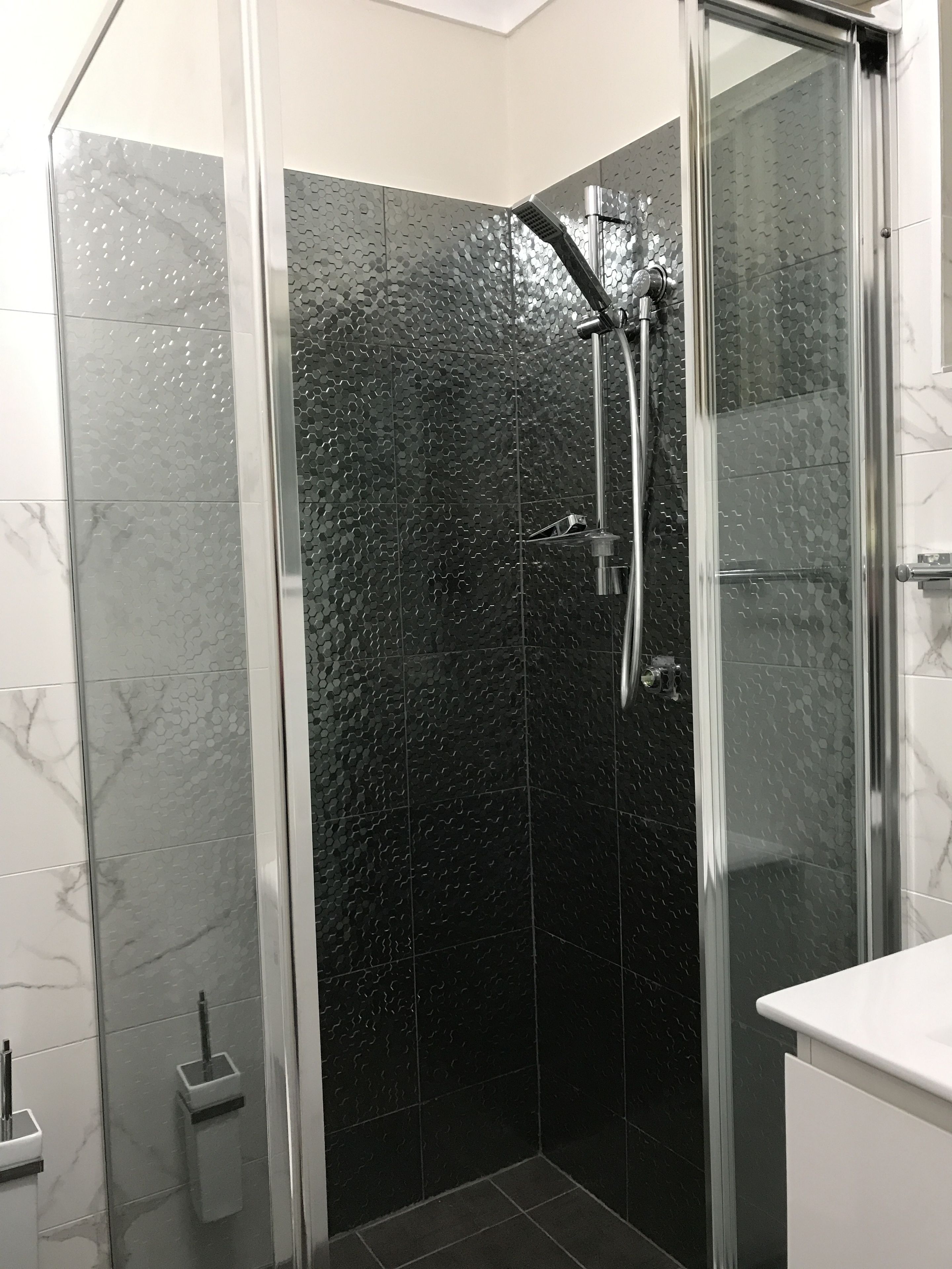 Un baño moderno con ducha envuelta en cristal, azulejos de mármol y encimera blanca.