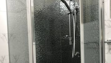 Un baño moderno con ducha envuelta en cristal, azulejos de mármol y encimera blanca.