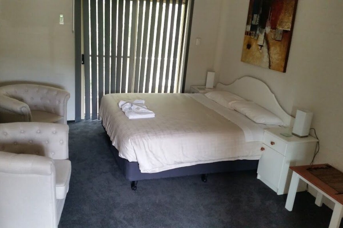 Una habitación de hotel con cama, una silla, mesita de noche y una pequeña mesa.