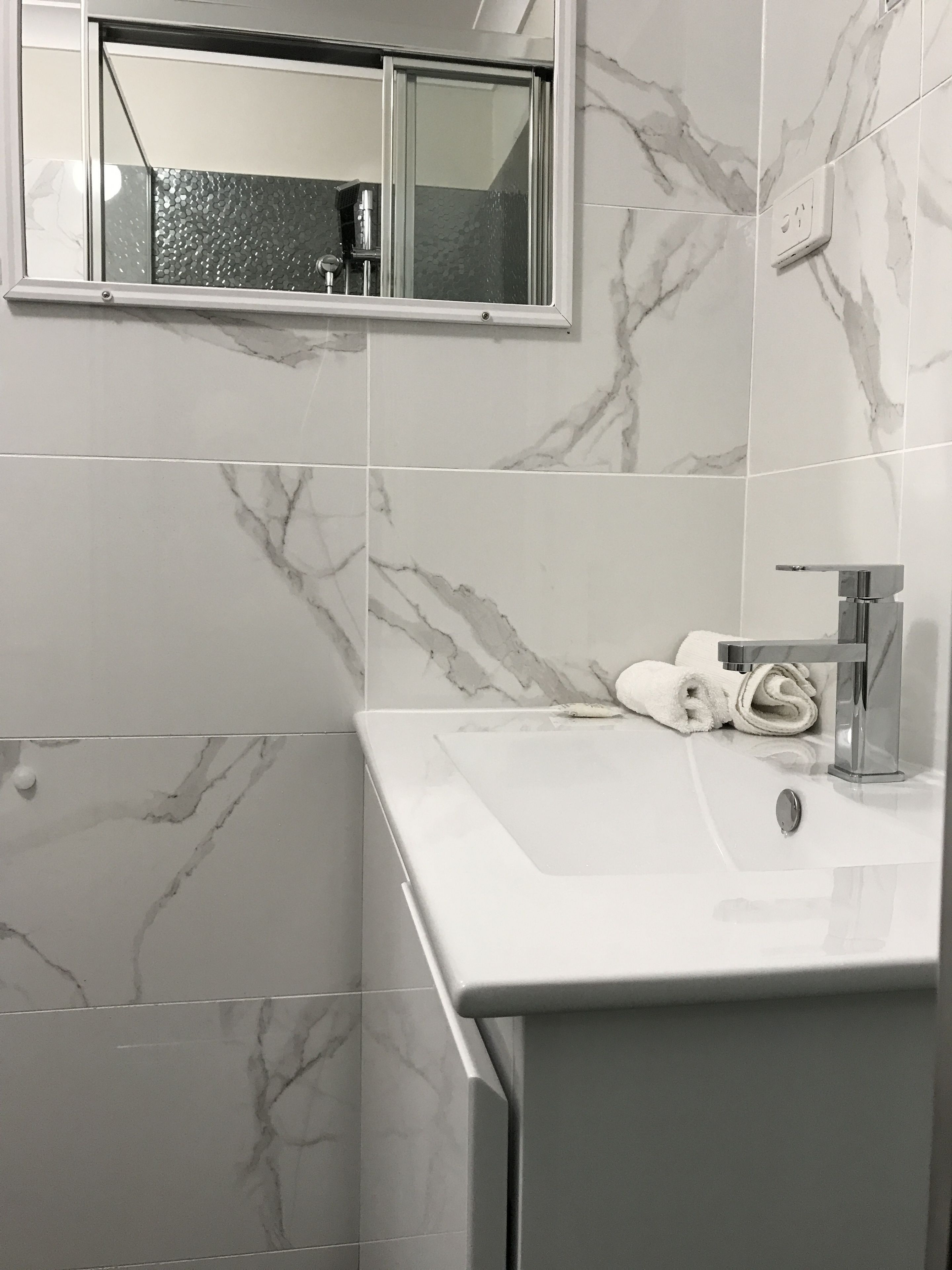 Un baño con lavamanos blanco, espejo y toalla.