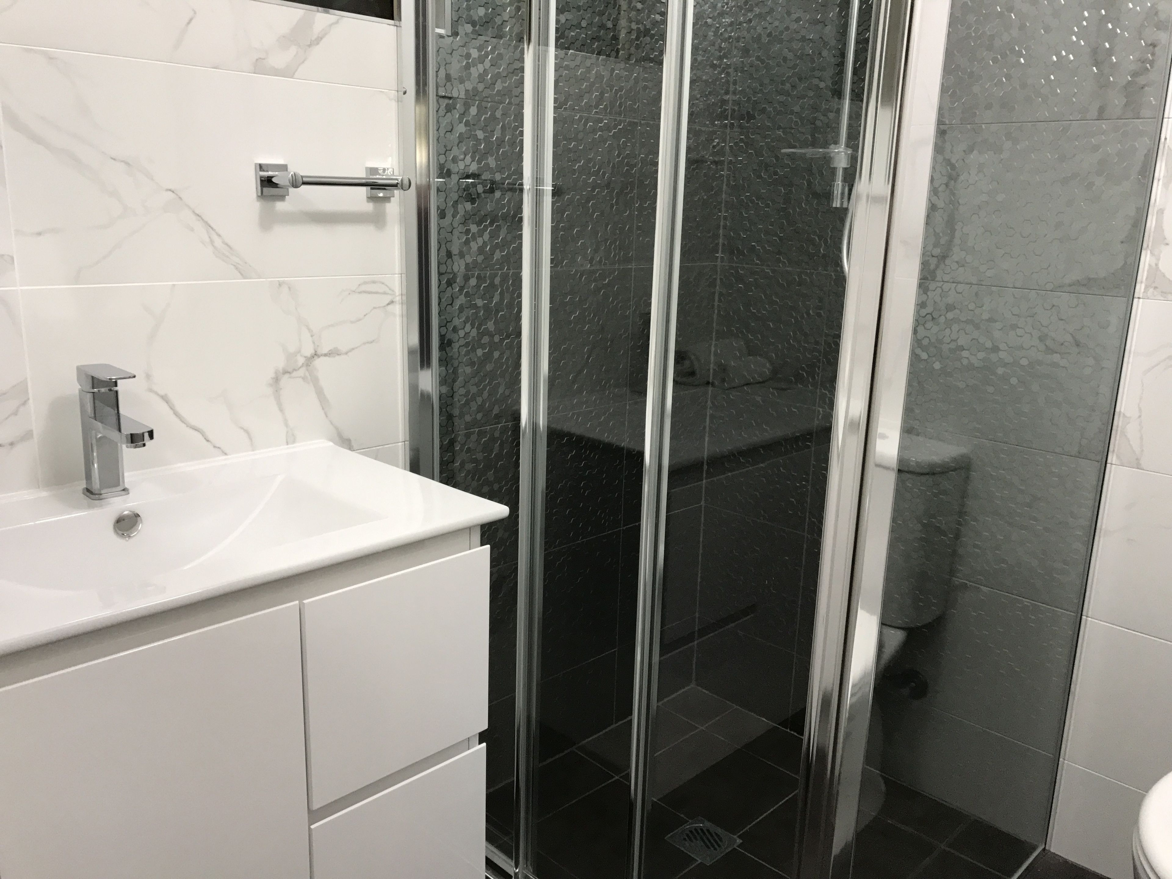 Un baño con lavamanos de mármol blanco, ducha con cerramiento de vidrio y retrete.