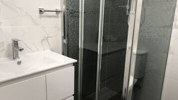 Un baño con lavamanos de mármol blanco, ducha con cerramiento de vidrio y retrete.