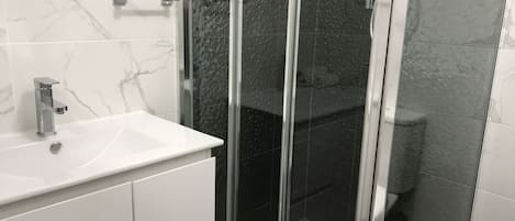 Un baño con lavamanos de mármol blanco, ducha con cerramiento de vidrio y retrete.