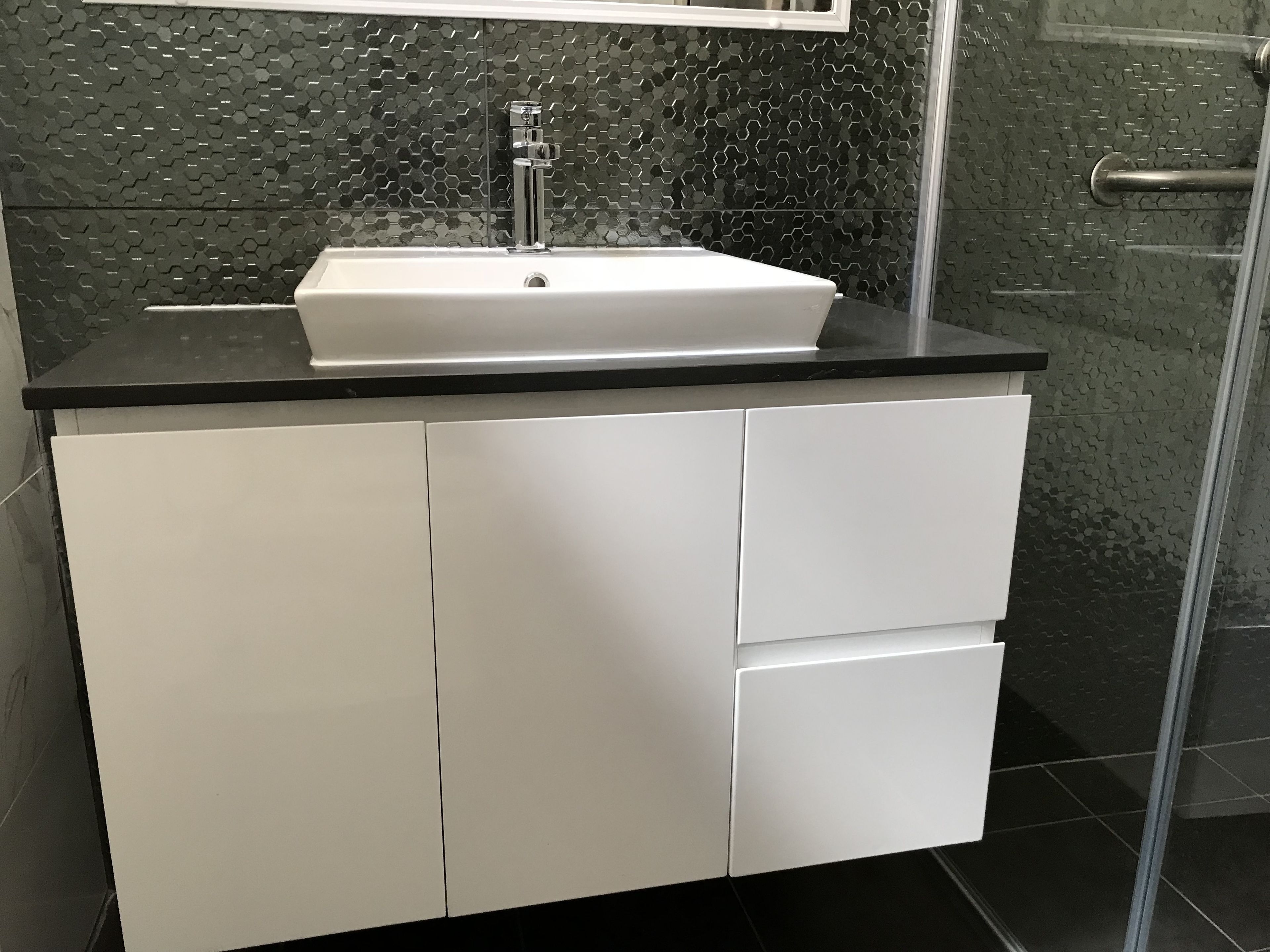 Un baño moderno con un lavamanos blanco, encimera negra y azulejos en la pared con un diseño hexagonal.