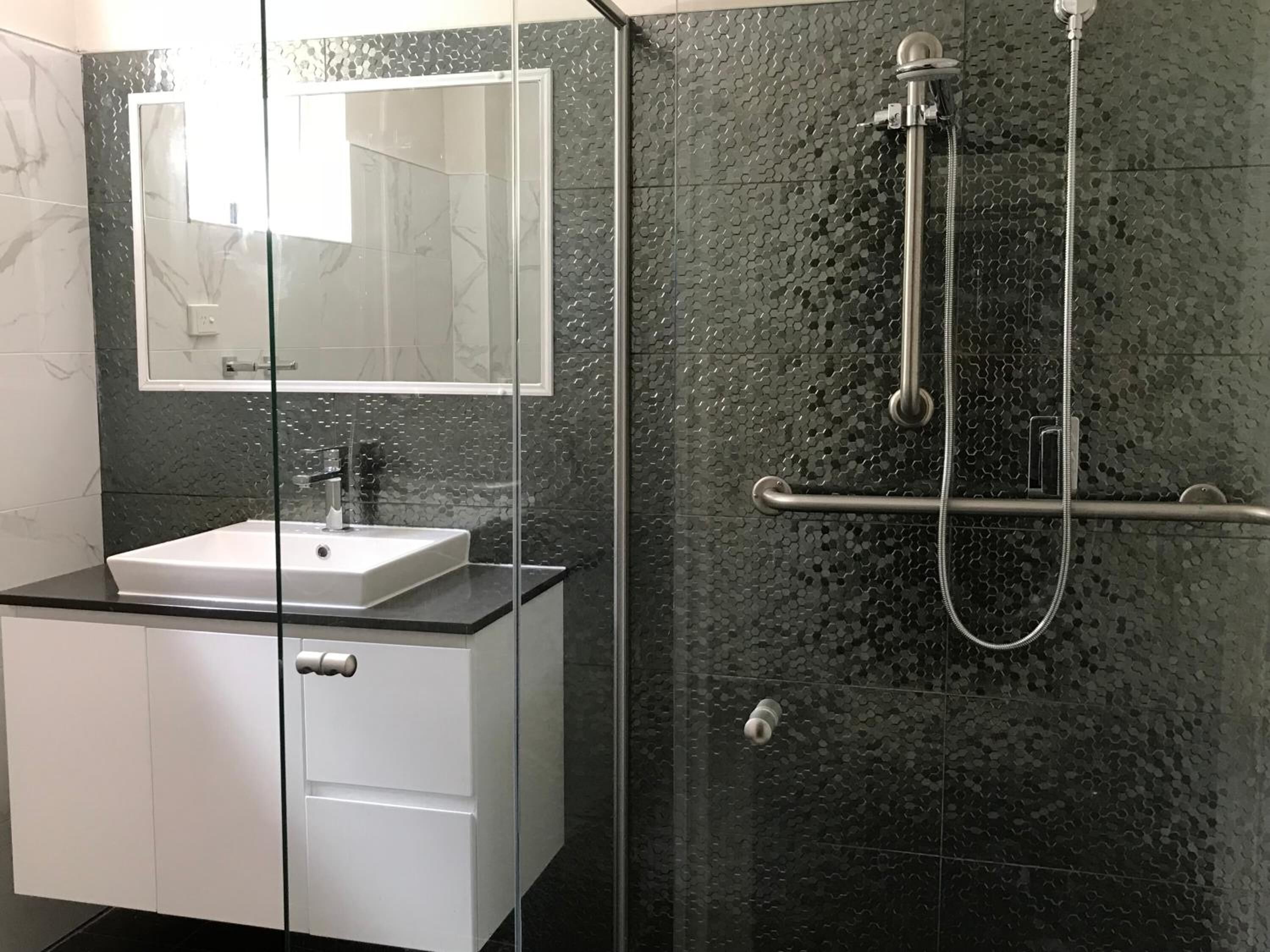 Un baño moderno con cabina de ducha de vidrio, un lavabo blanco y un espejo encima.