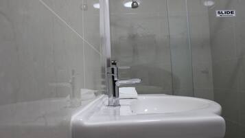 Une salle de bain avec un lavabo blanc, un robinet chromé et une douche à parois en verre.