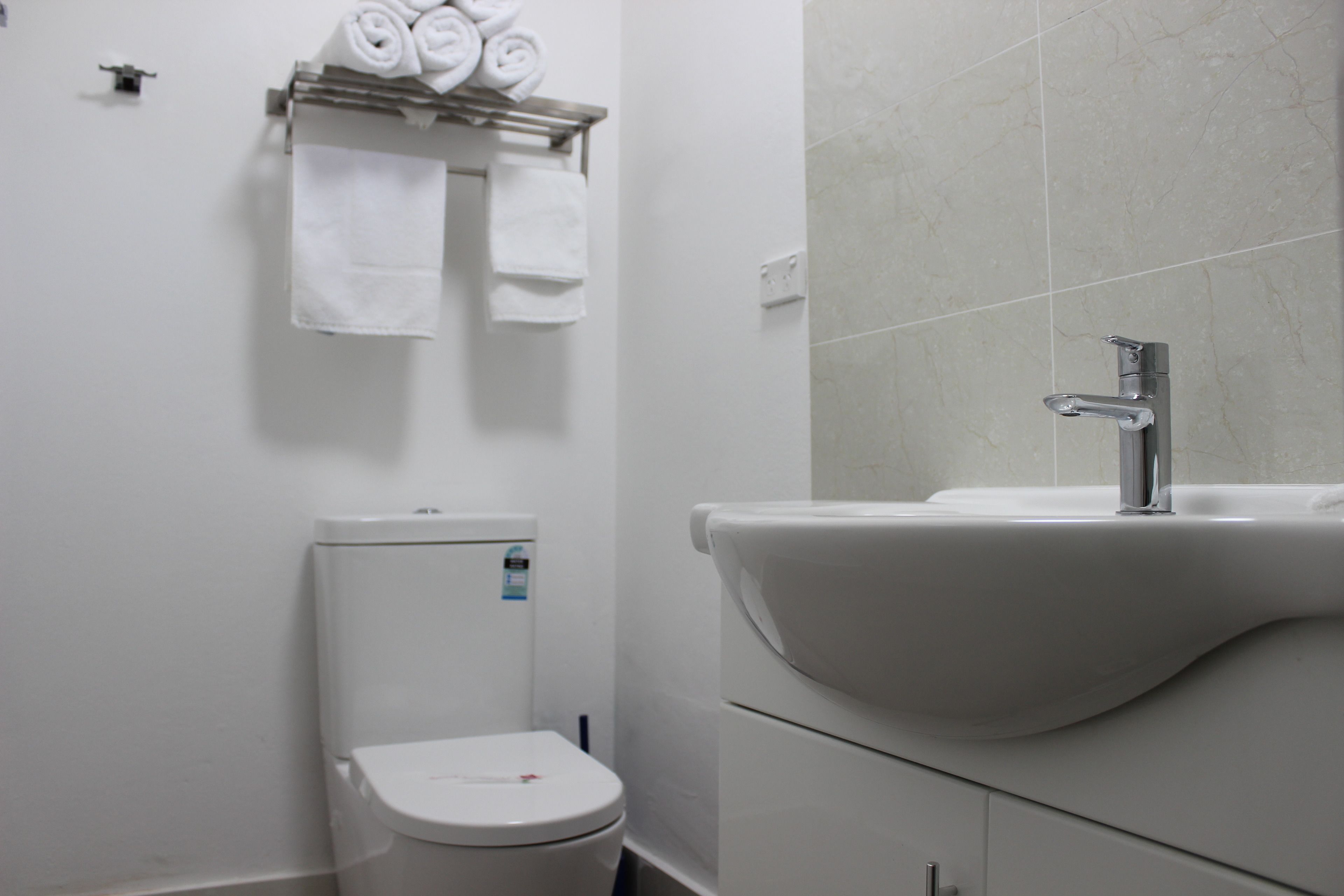 A bathroom with a toilet, a sink, and a towel rack with neatly rolled towels.