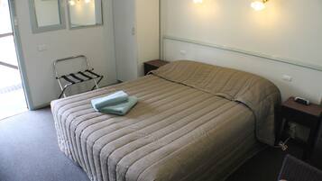 En pænt redt seng med et beige dynebetræk, et sengebord med lampe, og et spejl på væggen.