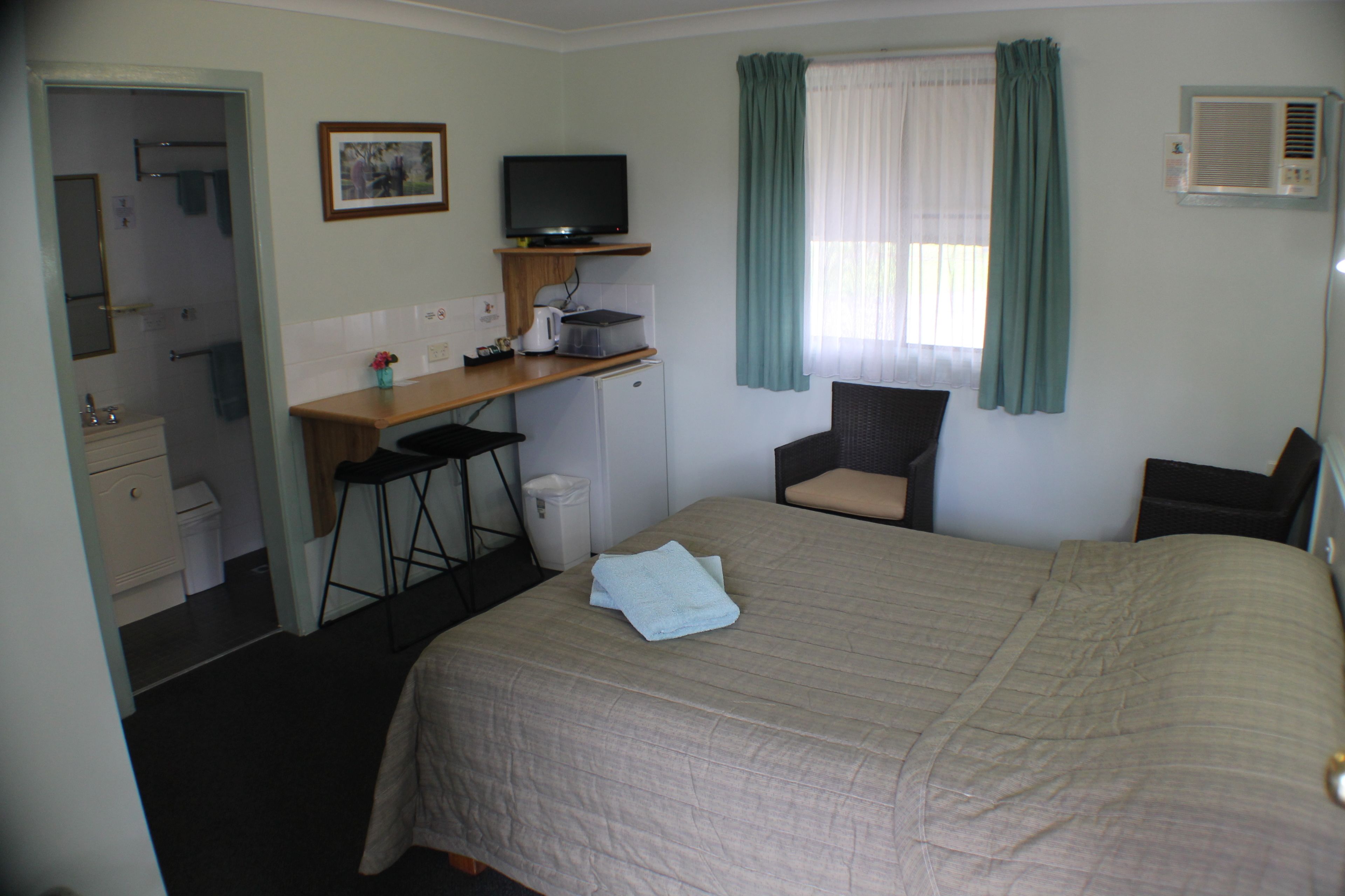Ein Hotelzimmer mit Bett, Schreibtisch inklusive Computer, Stuhl, einer kleinen Küchenzeile und Bad.