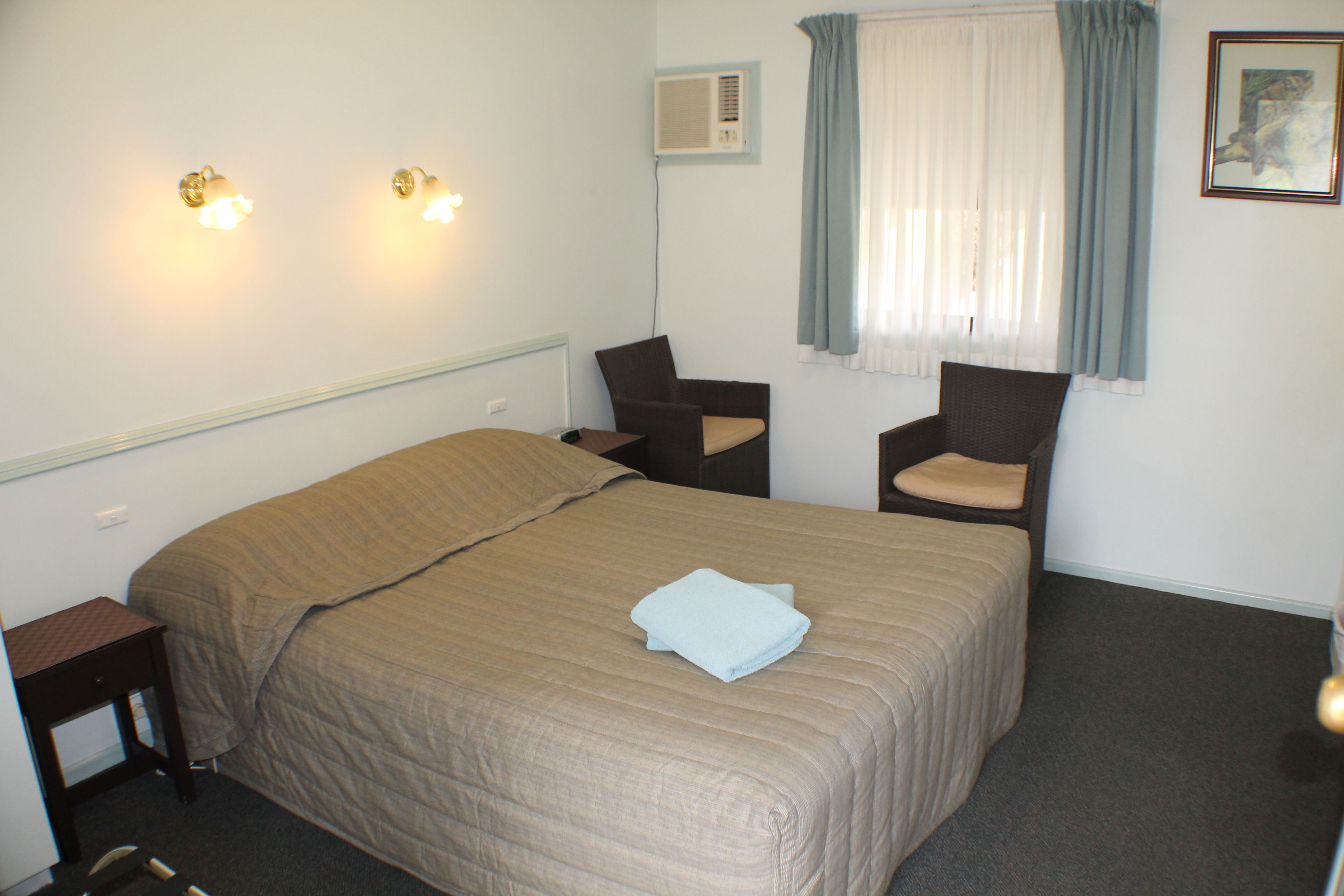 Ein Hotelzimmer mit einem Bett, zwei Sesseln, einem Nachttisch, einer Klimaanlage und einem Fenster mit Vorhängen.